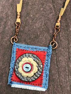 a blue and red square with a button on it's side hanging from a gold chain