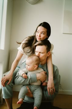 a woman holding a baby while sitting on top of a chair next to a man