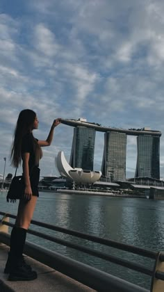 a woman standing next to the water looking at some buildings