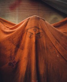 an orange cloth covering the face of a person with eyes drawn on it's side