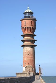 a tall brick tower sitting on the side of a pier next to the ocean in front of a blue sky