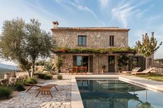 a stone house with a pool in the foreground and an olive tree on the other side