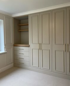 an empty room with white cupboards and shelves in the corner, next to a window