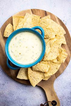 tortilla chips with dip in a blue bowl on a wooden board next to a spoon