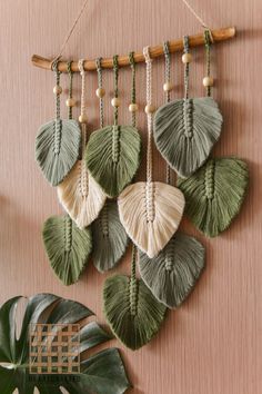 a wall hanging made out of green leaves and white beads on a wooden board next to a potted plant