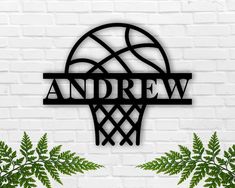 a basketball hoop with the word andrew on it next to some green plants in front of a white brick wall