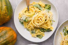 two plates of pasta with spinach and cheese next to pumpkins on the table