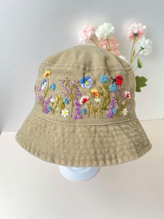 a tan hat with flowers on it sitting on top of a white table next to pink and blue flowers