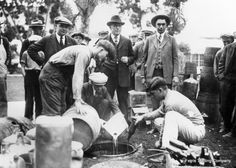 an old black and white photo of men in suits pouring water from buckets into barrels