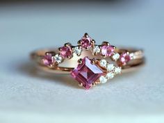 a pink diamond ring sitting on top of a white table next to a pair of diamonds