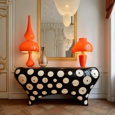 a black and white table with orange lamps on it in front of a large mirror