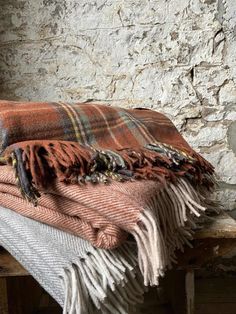 a plaid blanket sitting on top of a wooden bench next to a brick wall and window