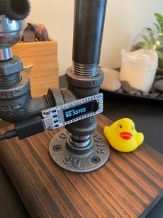 a yellow rubber duck sitting on top of a wooden table next to a metal pipe