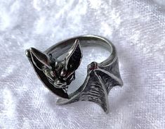 A sinister, vampiric creature, thirsting for unsuspecting prey to carelessly cross their path. Pay homage to the creature of the night with this antiqued pewter statement ring. This ring is adjustable! A bat wraps its wings around your finger. Made by Kiss of a red rose with inspiration from Alchemy England. The ring comes with a gift pouch. Vampire Ring Aesthetic, Vampire Rings, Vampire Jewelry Rings, Adjustable Gothic Skull Ring, Adjustable Gothic Skull Ring Collectible, Bat Ring Jewelry, Vampire Ring, Black Bat Jewelry, Victorian Bat Jewelry