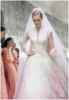 a woman in a wedding dress and veil walking down the runway with other people behind her