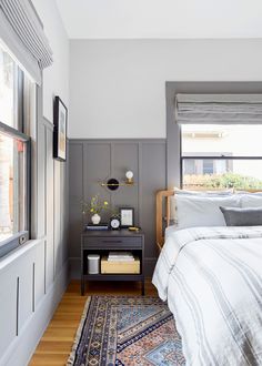 a bedroom with gray walls and white bedding, rugs and window sill