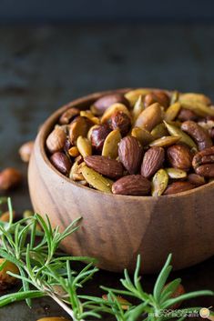 a wooden bowl filled with nuts on top of a table next to rosemary sprigs