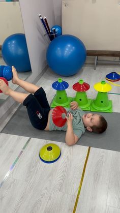 a young boy laying on the floor playing with some balls and toys in front of him