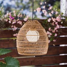 a rattan light hanging from a wooden fence with pink flowers in the back ground