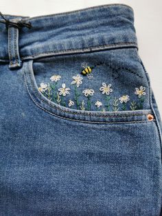 a pair of jeans with embroidered flowers on the side and a bee in the pocket