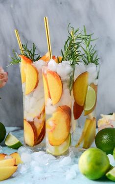 two tall glasses filled with lemonade and limes next to some sliced oranges