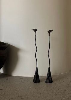 two black vases sitting next to each other on the floor in front of a white wall