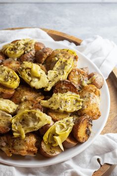 a white plate topped with fried potatoes covered in green sauce and cheese on top of a wooden cutting board