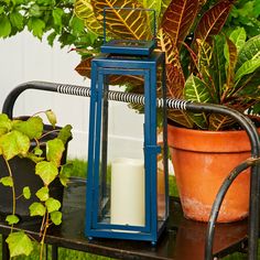 a blue lantern sitting on top of a table next to a potted plant with a candle in it