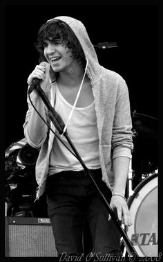 a young man holding a microphone while standing next to a drum and singing into a microphone