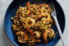 a blue plate topped with pasta and shrimp next to a fork on top of a table