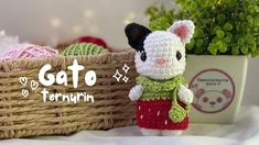 a small crocheted cat in a red dress next to a basket with balls of yarn