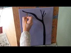 a person is holding a pencil in front of a painting on a easel with a tree