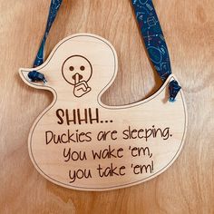 a wooden duck hanging on a table with a blue lanyard around it's neck that says, shh ducks are sleeping you wake em, you take em, you take em