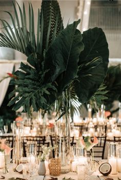 a table topped with lots of candles and greenery next to tall vases filled with flowers