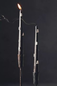 two black candles with one lit and the other turned upside down, on a dark background