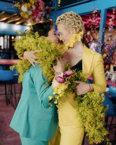 two women hugging each other in front of a table with blue chairs and flowers on it