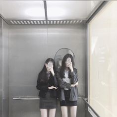 two women standing in front of a mirror on the side of a wall with their hands to their faces