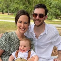 a man and woman sitting on a bench with a baby in their lap, smiling at the camera