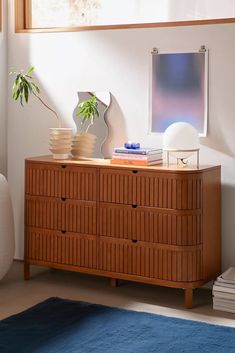 a wooden dresser sitting in a living room next to a blue rug and potted plant