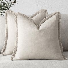 two pillows sitting on top of a couch next to a vase with flowers in it