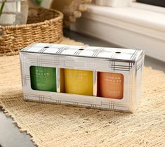 three candles in a box sitting on a table next to a basket and window sill