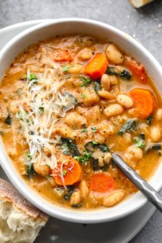 a white bowl filled with soup and topped with parmesan cheese, carrots and spinach