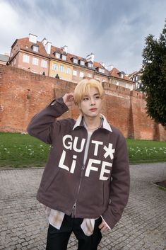 a young man standing in front of a brick wall wearing a brown jacket with the words gutt life on it