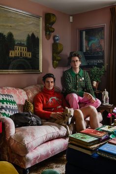 two people sitting on a couch in a living room with pink walls and colorful furniture