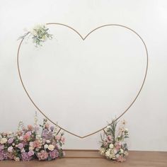 a heart shaped frame with flowers and greenery in front of it on a table