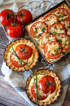 four pies with tomatoes and herbs in them sitting on a table next to some cherry tomatoes