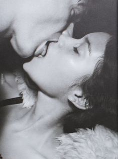 a man kissing a woman's face with her nose close to her chest, in front of a black and white photo