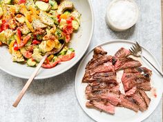 two plates with steak and vegetables on them next to a bowl of salt and pepper