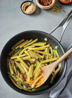 green beans and sesame seeds in a skillet with wooden spoons on the side