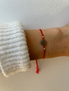 a woman's arm wearing a red string bracelet with a green bead on it